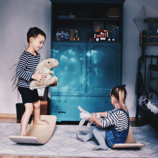 Two children balancing on wooden balance boards with grey felt, playing together indoors