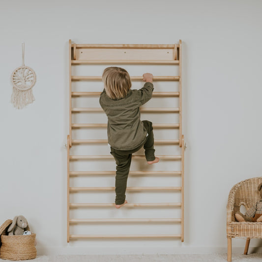 Child climbing Swedish wall mounted on white wall with wicker basket and macrame decoration nearby