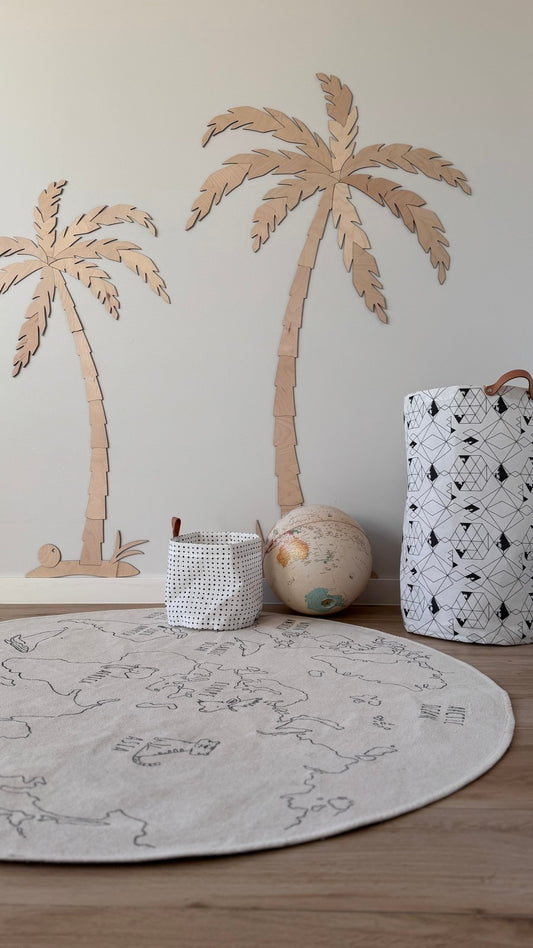 Two hand-cut wooden palm trees in natural plywood displayed on a nursery floor with toys