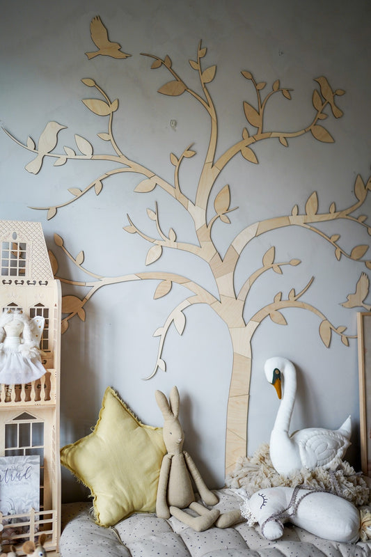 Wooden tree wall decoration with birds and leaves installed in a nursery above soft toys and furniture